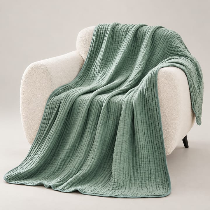 Sage green cotton muslin throw draped over a white armchair